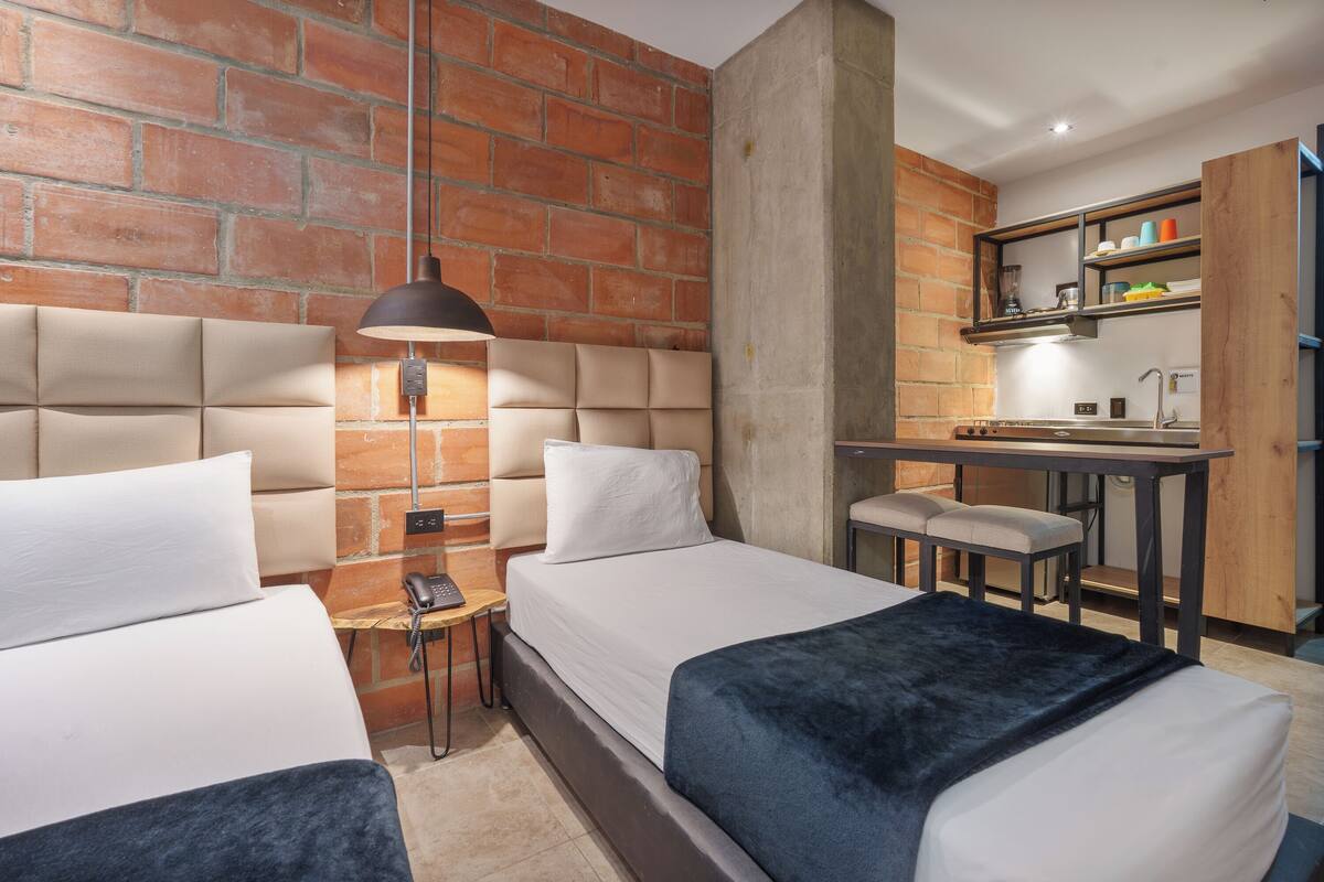Una habitación de hotel con pared de ladrillo, dos camas, un escritorio y una pequeña zona de estar.