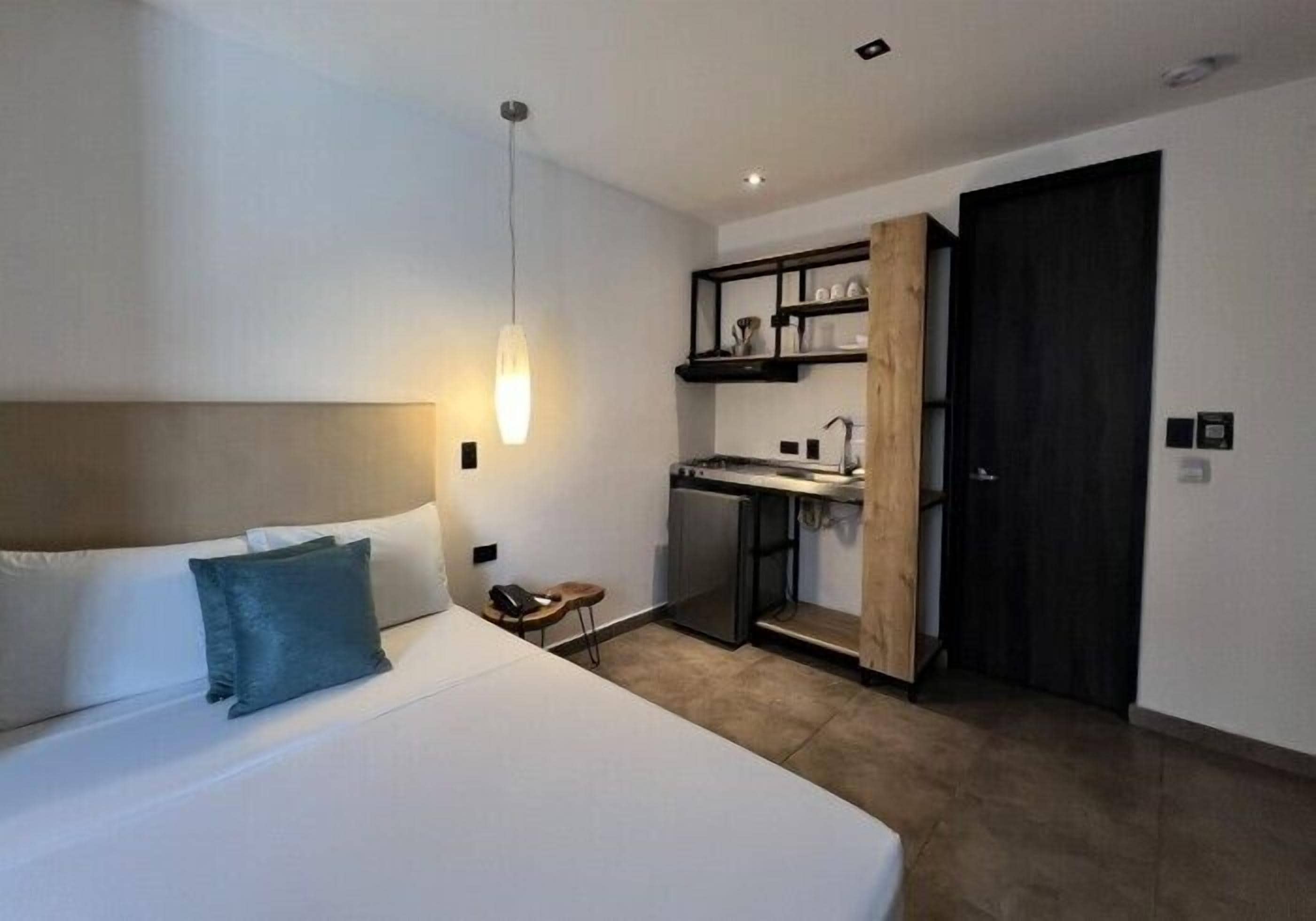 Quarto de hotel moderno com uma cama, uma kitchenette pequena e uma porta de madeira.