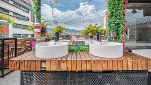 Un bar situé sur le toit, avec deux éviers blancs, des tables en bois et une vue sur le paysage urbain.