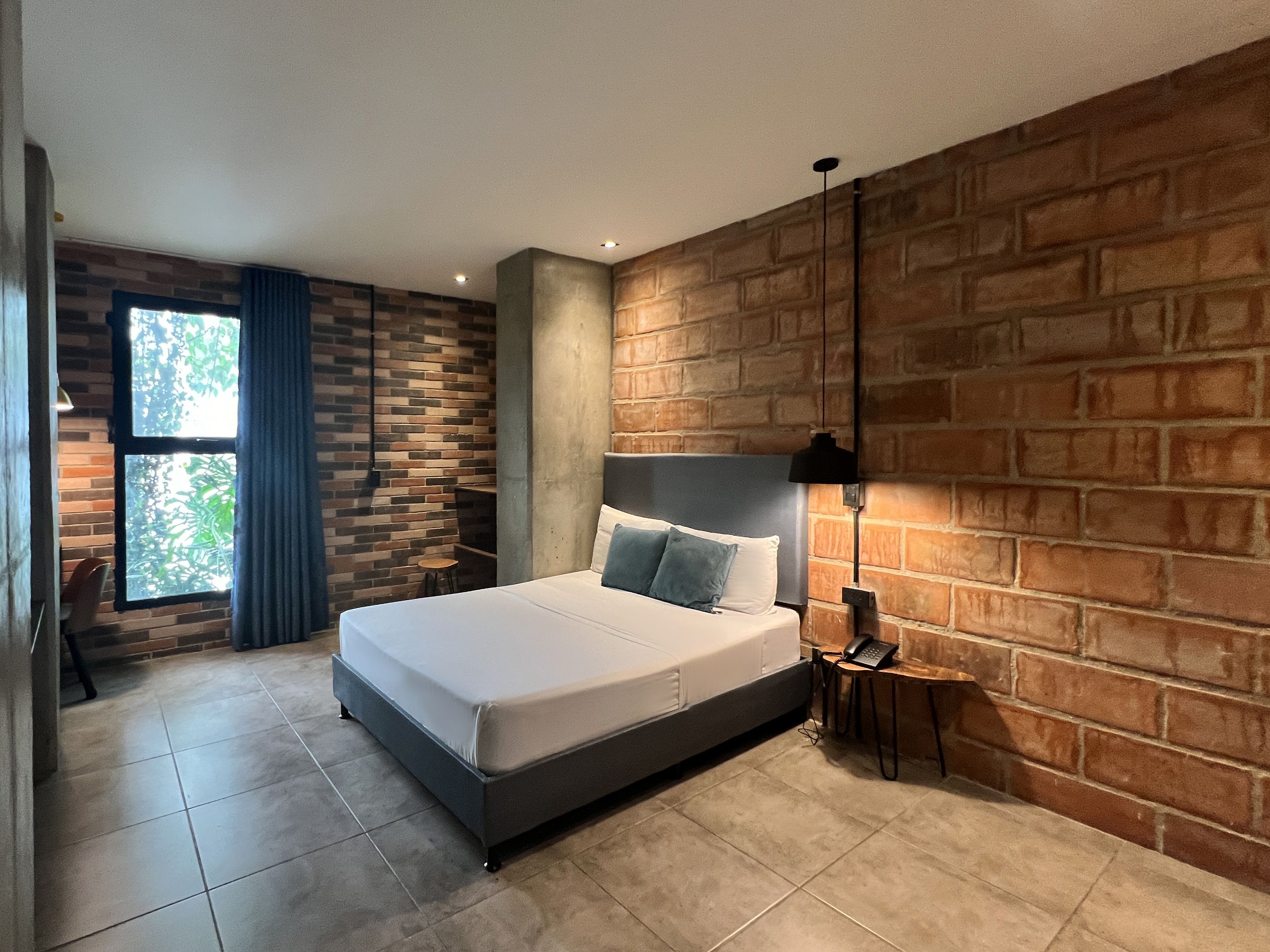 Une chambre moderne avec un mur en briques, un grand lit, une petite table avec une lampe et une fenêtre avec des rideaux.