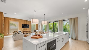 A modern kitchen with a large island, wooden accents, and a view of greenery outside.