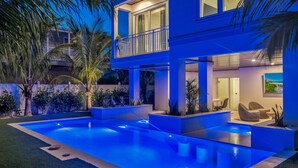Ein modernes, zweistöckiges Haus mit Schwimmbad, Sitzgelegenheiten im Freien und einem Balkon.