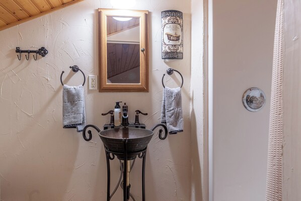 A bathroom with a wooden ceiling, a mirror, a sink with two towel racks, and a decorative wall piece. - Veale Creek Retreat on Possum Kingdom Lake (Graham)
