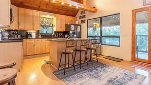 Una cocina moderna con armarios de madera, una zona de bar con taburetes y ventanas amplias con vistas al exterior.