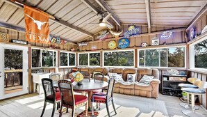 Un patio techado al aire libre con zona de comedor, sofá de cuero y varios carteles de cerveza.