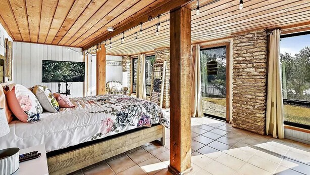 Un dormitorio con techo de madera, una cama grande, un televisor y una pared de piedra.