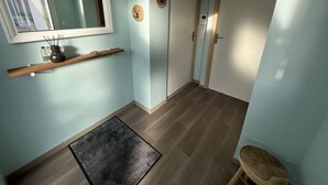 Un corridoio con pareti azzurrognole, pavimento in legno, un tappeto nero, una mensola in legno con un vaso e una bottiglia, e due porte.