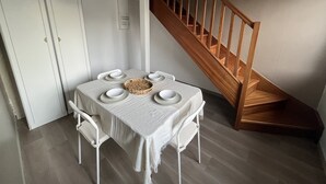 Zona pranzo con una scala in legno, sedie bianche e un tavolo apparecchiato con piatti e un cesto di vimini.