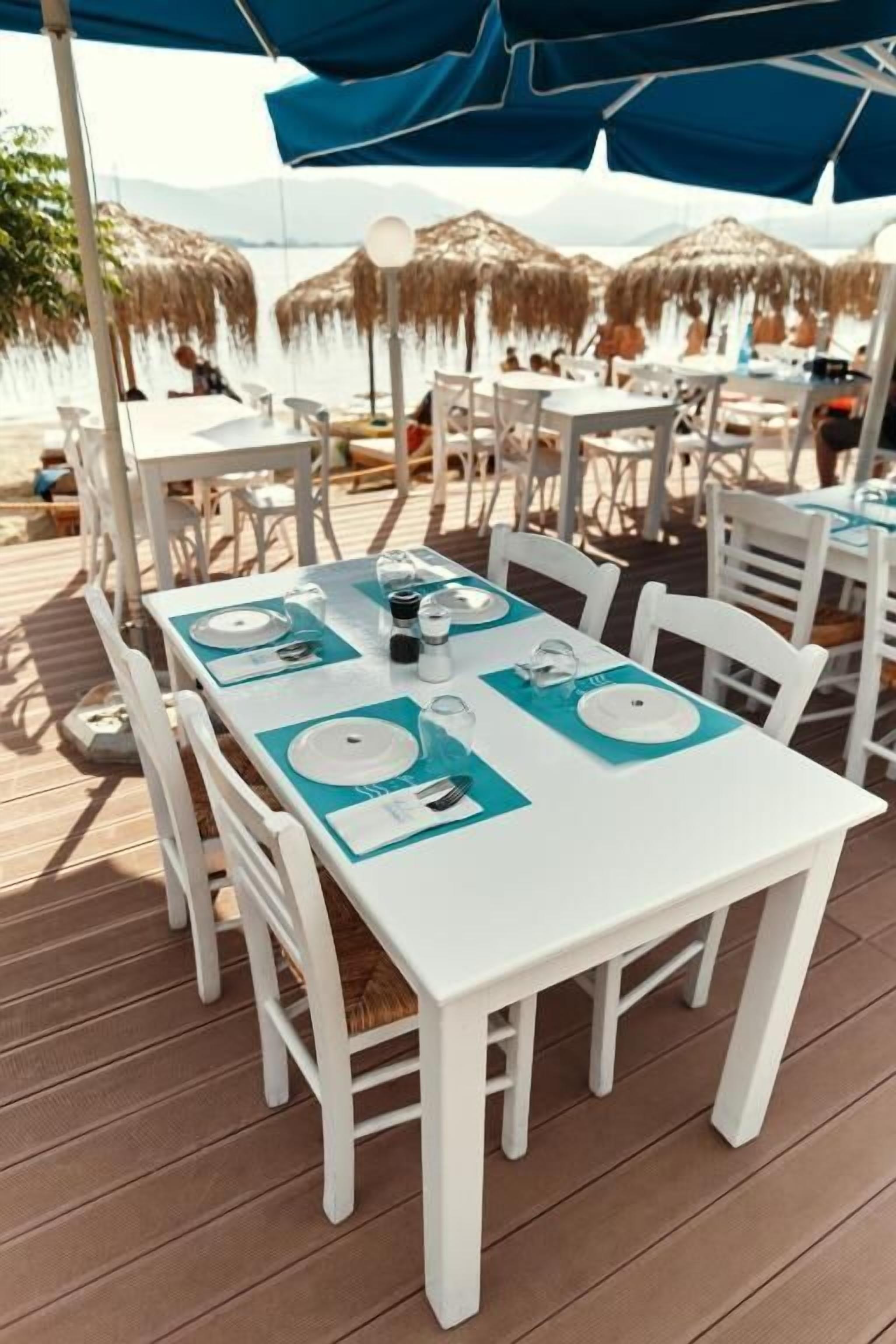 Een terras met witte tafels en stoelen, waarvan sommige blauwe tafelonderleggers hebben.