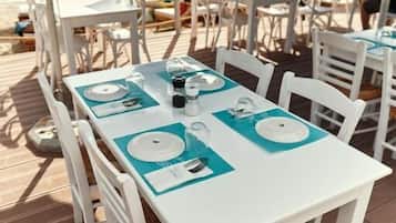 Een terras met witte tafels en stoelen, waarvan sommige blauwe tafelonderleggers hebben.