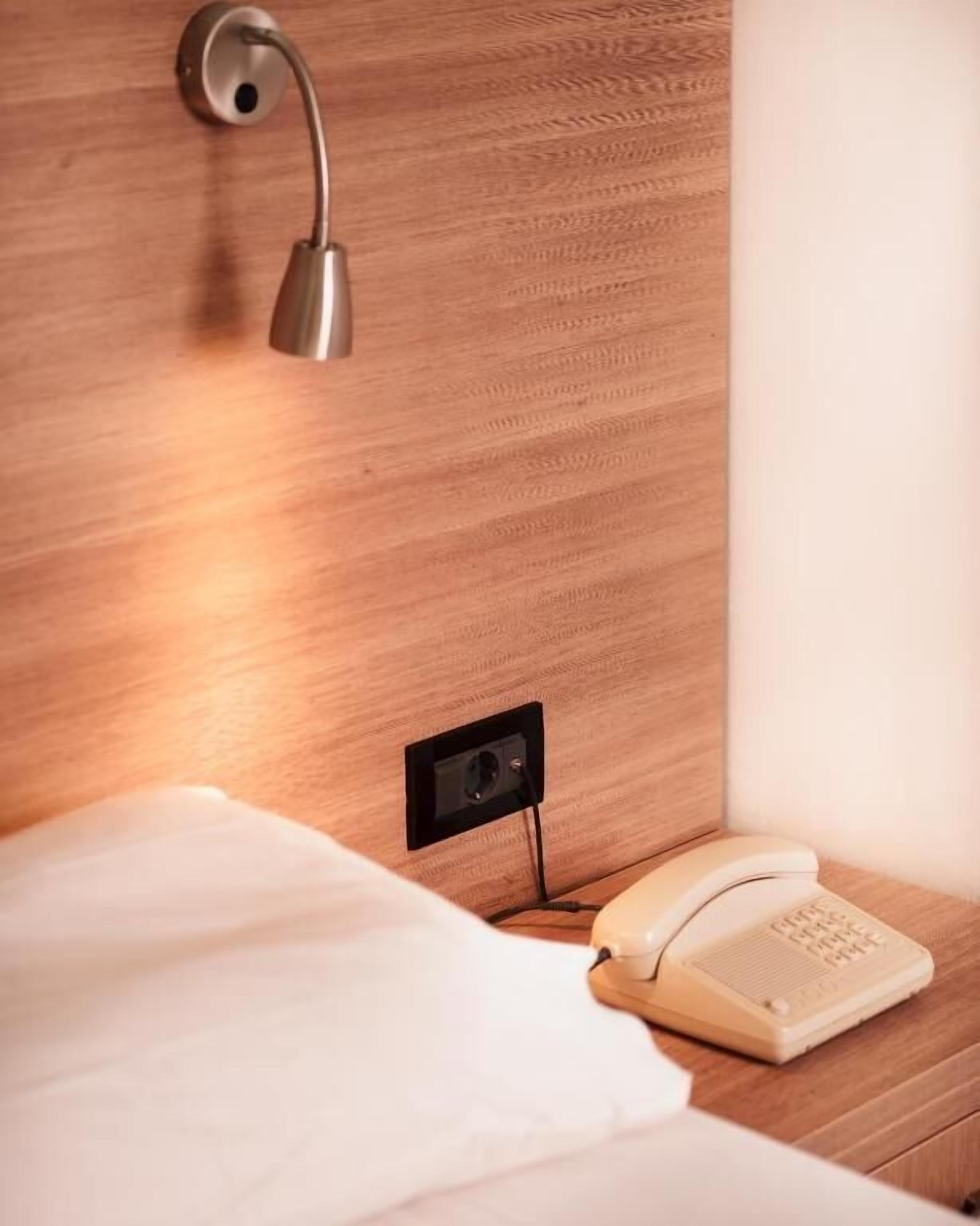 Un lit bien fait, avec une couette blanche et un téléphone sur une table de chevet en bois.