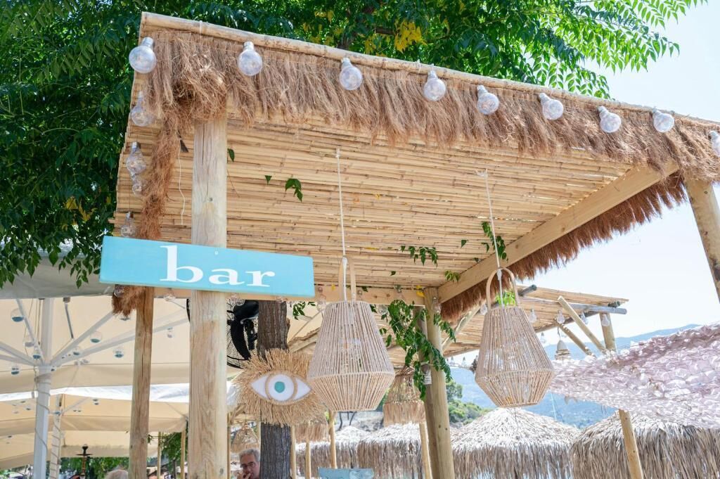 A rustic outdoor bar area with a thatched roof, hanging light fixtures, and woven decorations.
