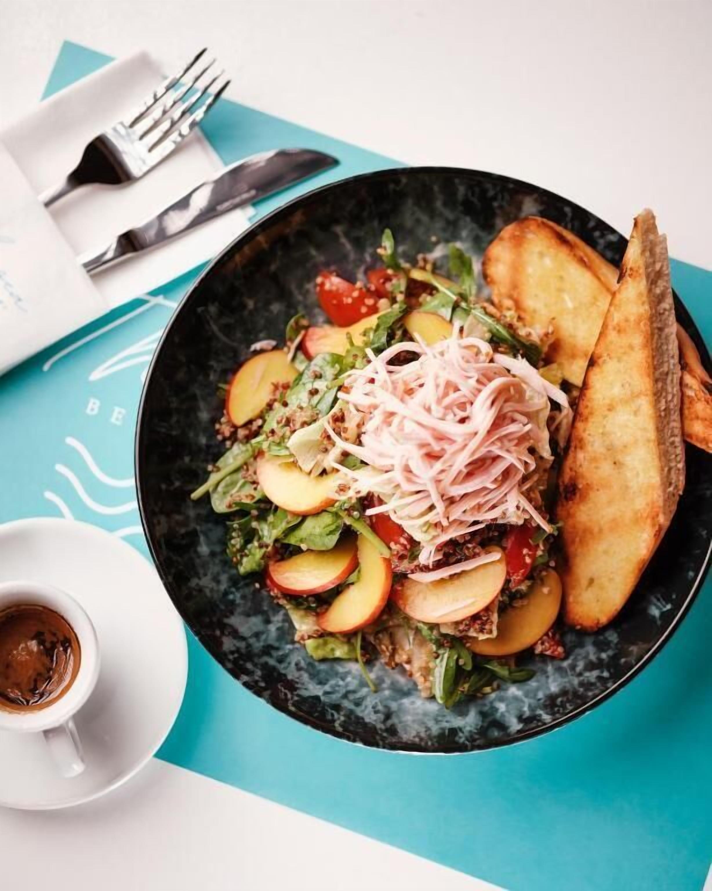 A plate of food with a salad, sliced apples, and a meat topping, accompanied by toasted bread and a small cup of sauce.