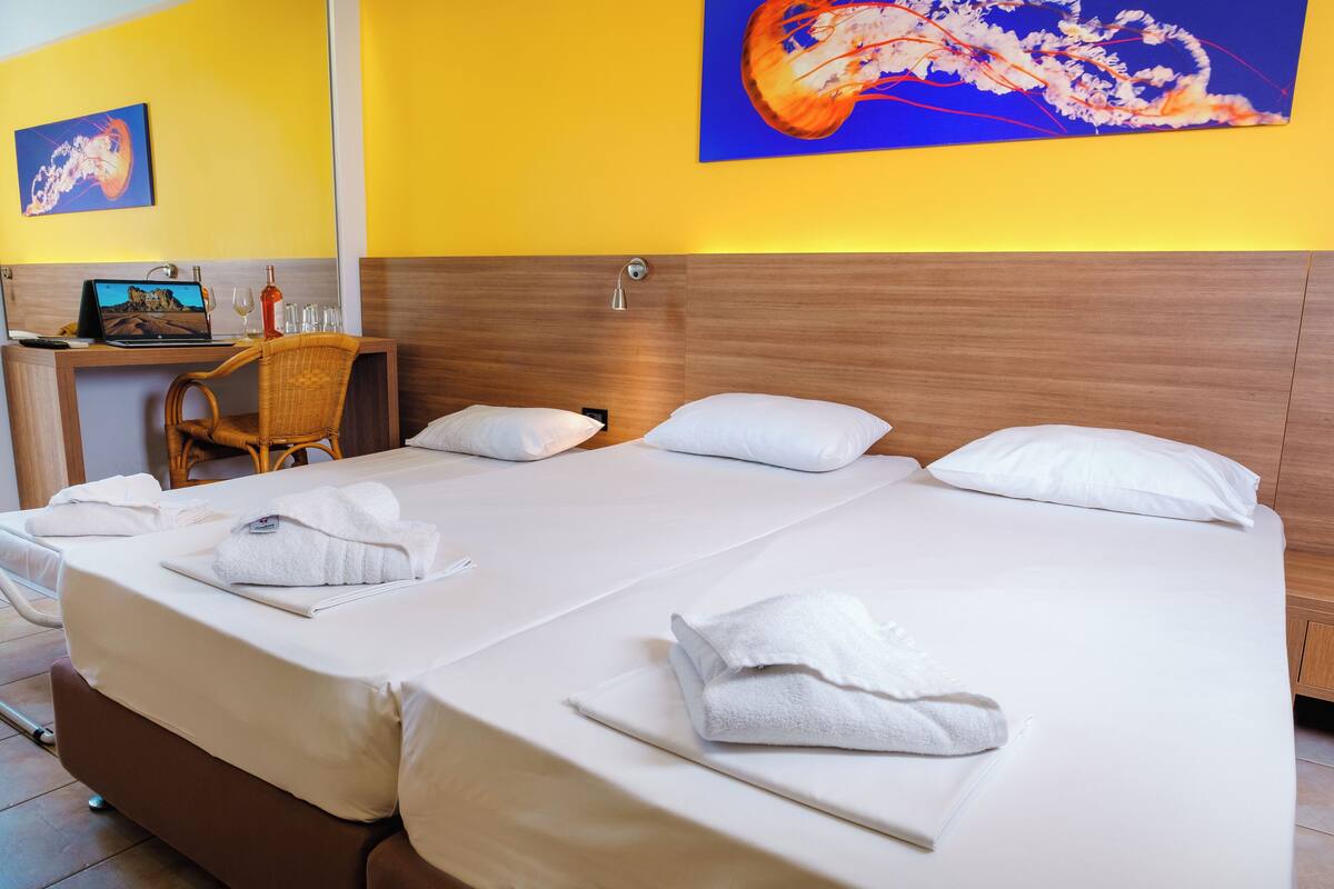 A hotel room with two beds, a desk with a laptop, and a chair.