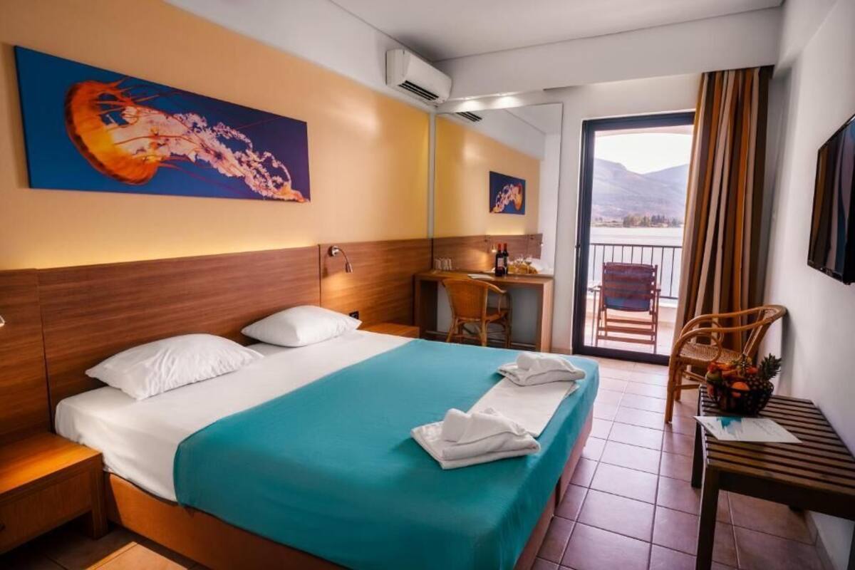 A hotel room with a bed, a desk, a chair, and a balcony with a view of the mountains.