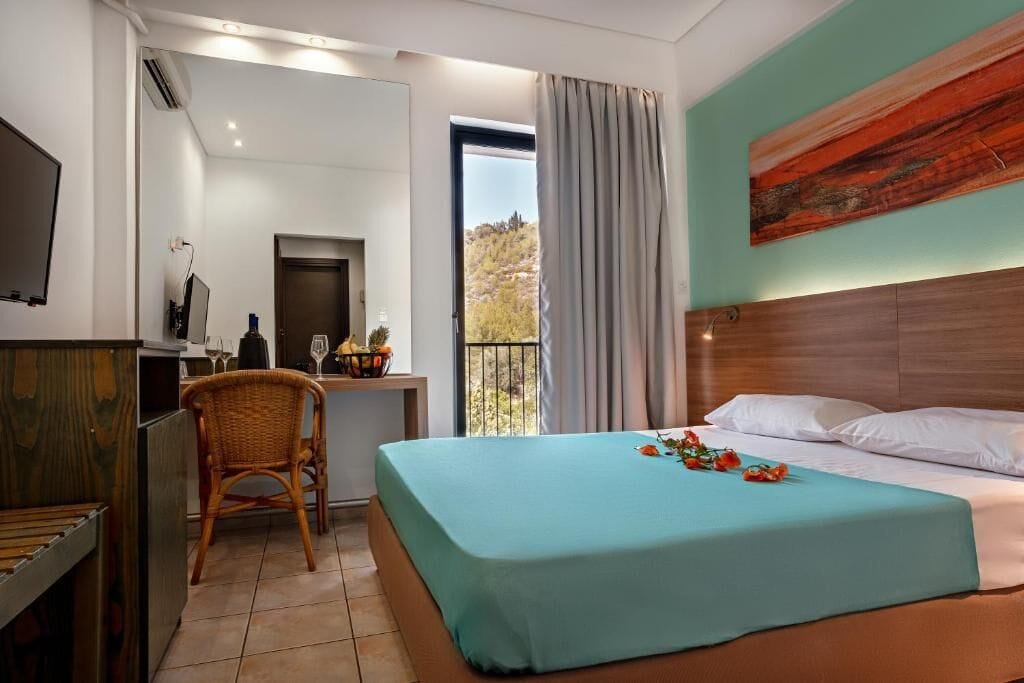 Habitación de hotel con cama, escritorio, silla, televisor y ventana con cortinas.