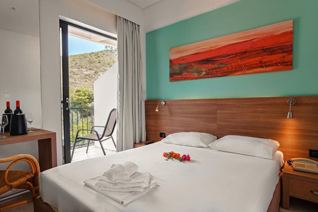 Habitación de hotel con cama, escritorio y silla, balcón con vistas y un cuadro en la pared.