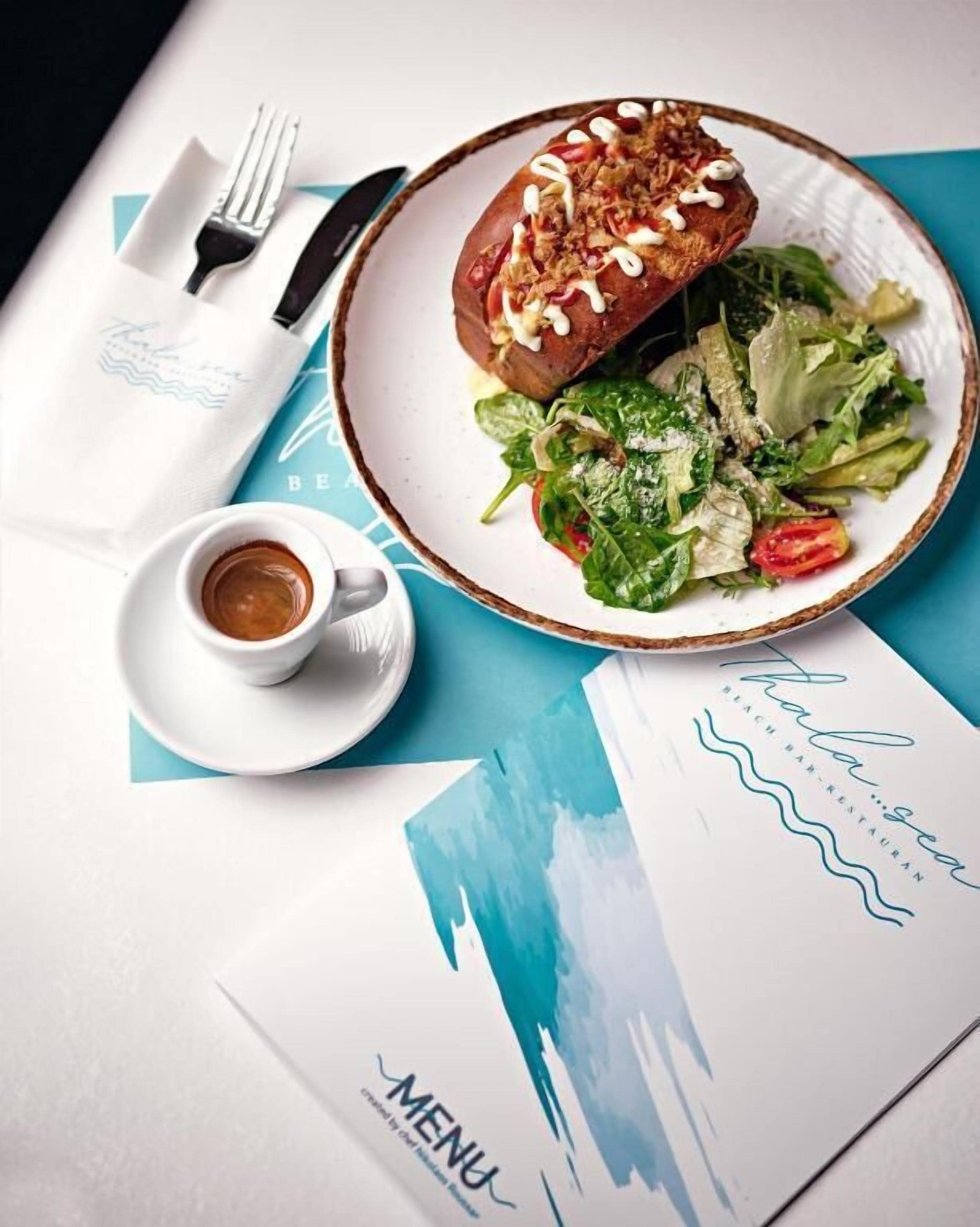 A meal with a sandwich, salad, and a cup of coffee on a table with a menu.