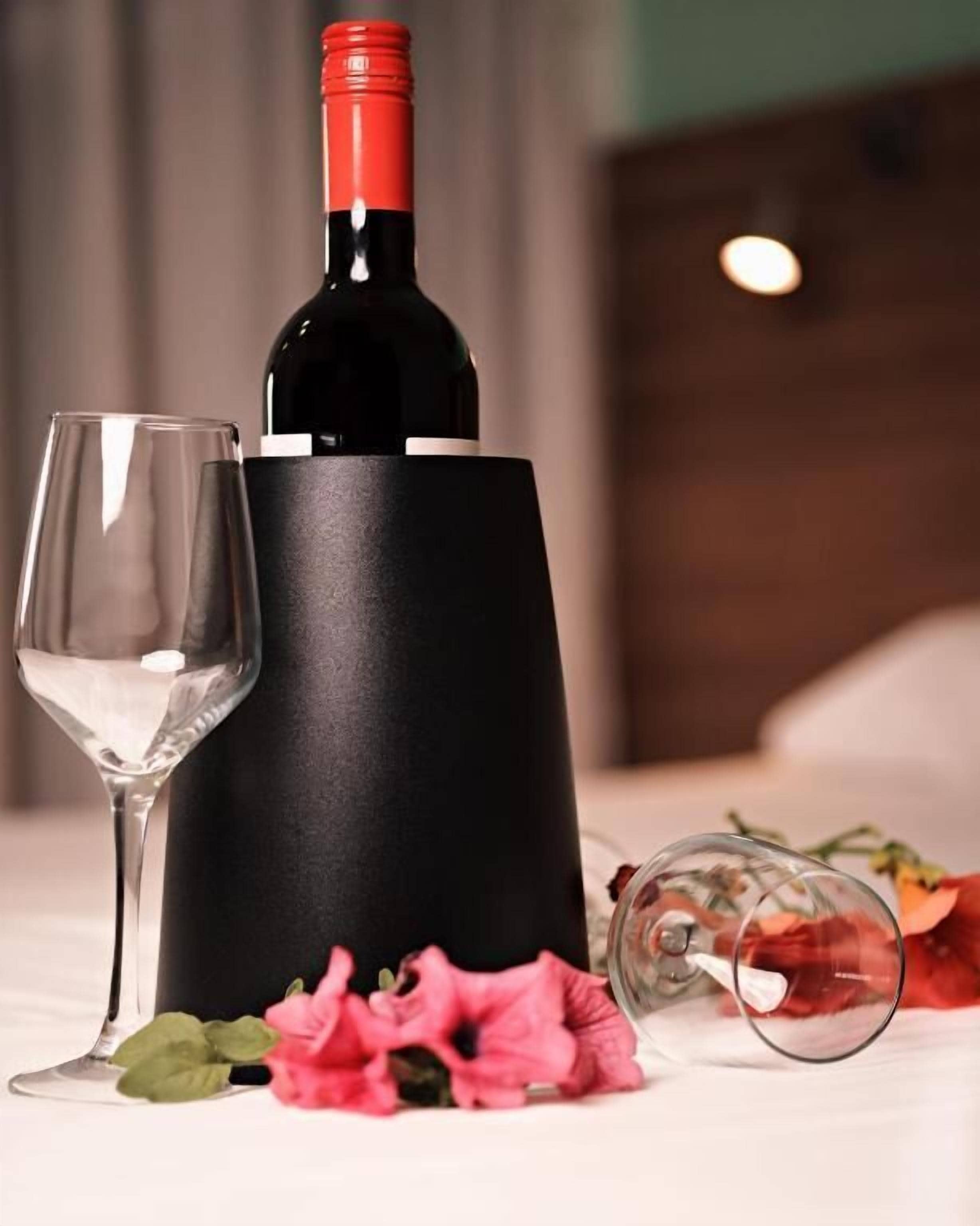 Uma garrafa de vinho, uma taça de vinho e um jarro sobre uma mesa com flores.