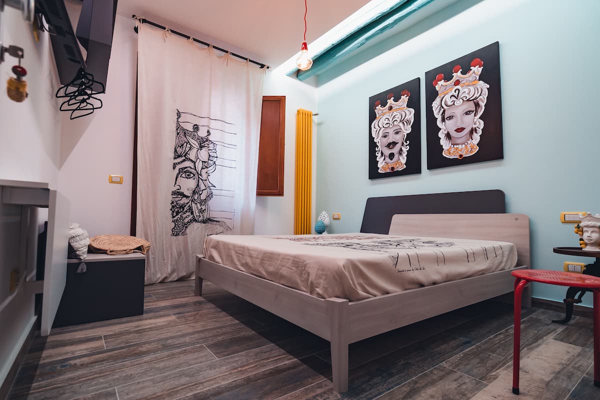 A bedroom with a bed, a nightstand, a red chair, and artwork on the walls.