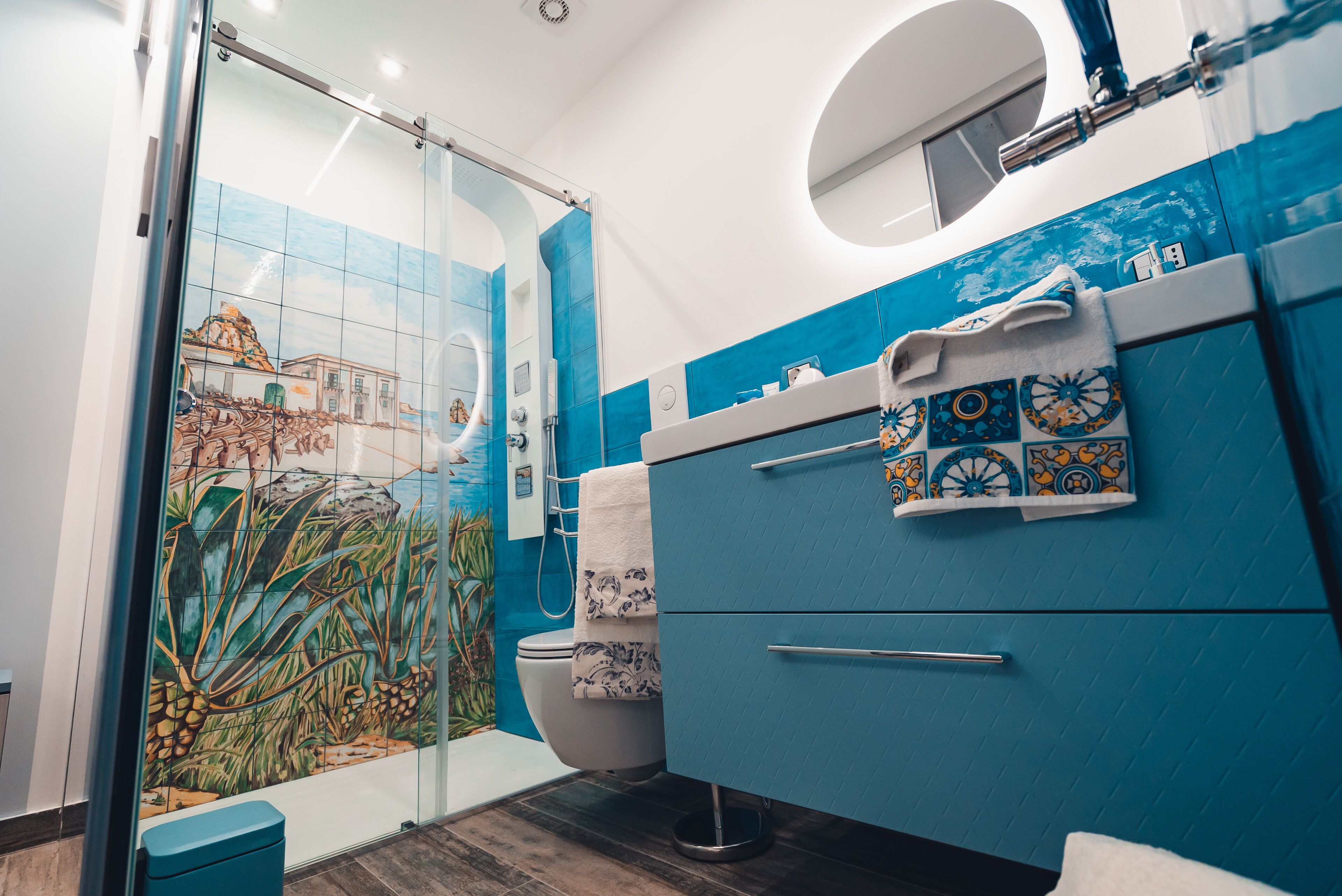 A bathroom with a glass shower enclosure, a toilet, and a sink with a blue cabinet and decorative tiles.