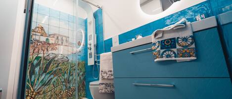 A bathroom with a glass shower enclosure, a toilet, and a sink with a blue cabinet and decorative tiles.