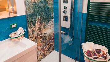 Un baño con ducha envuelta en vidrio, un lavabo blanco, un mueble de tocador de madera y una pared decorada con azulejos.