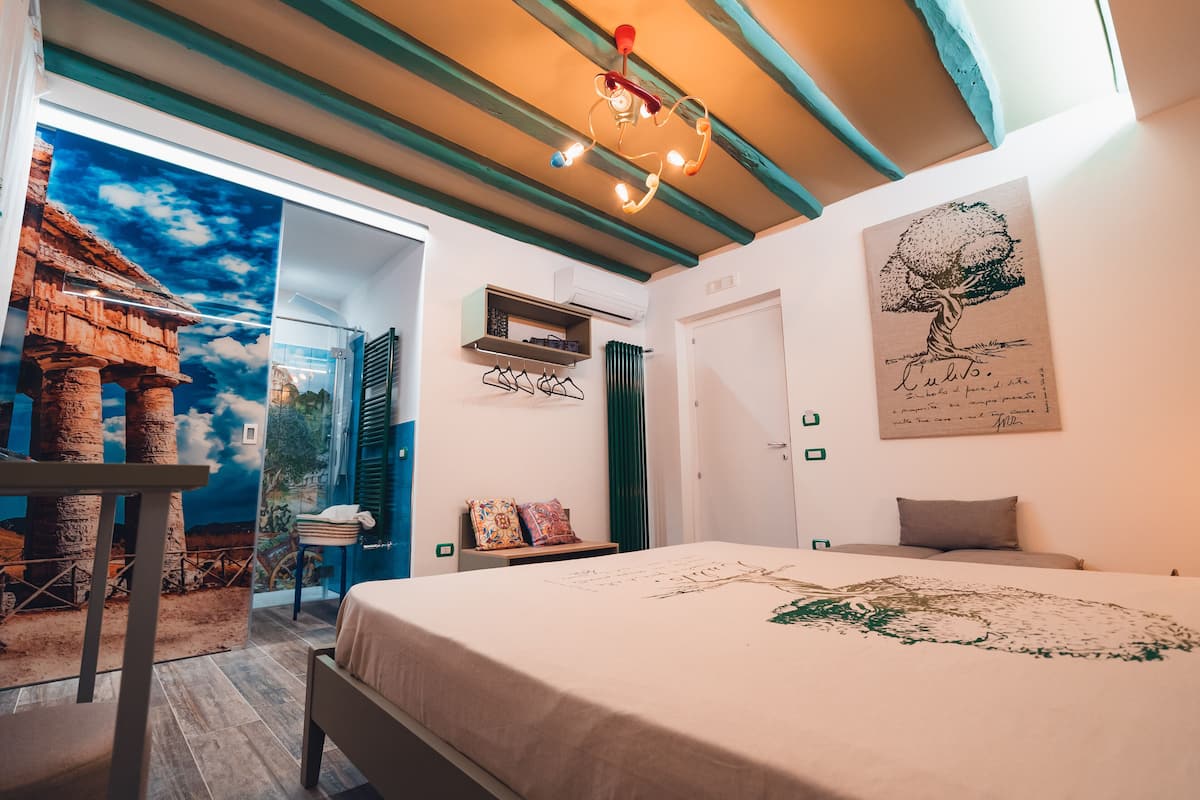 A bedroom with a bed, a mural of a temple, a ceiling light, and a door.