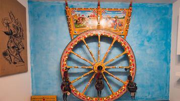 A large, ornate wheel with intricate designs and figures, mounted on a blue wall.