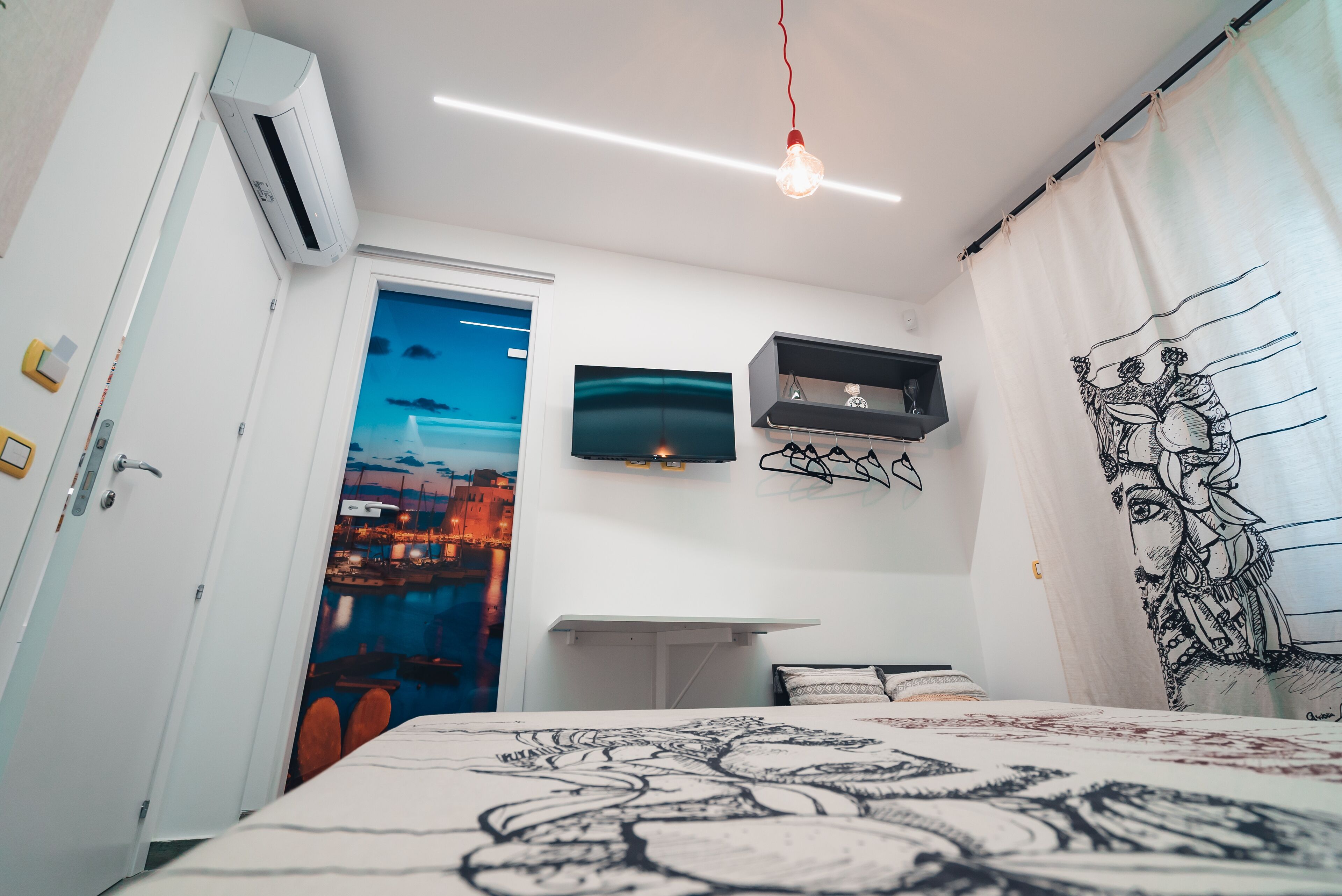 Un dormitorio con cama, estante en la pared, televisor de pantalla plana y puerta que da a otra habitación.
