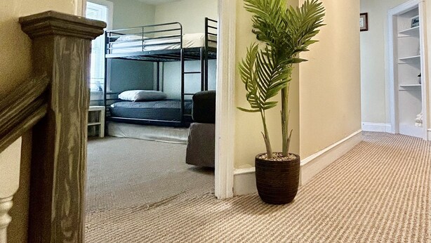 A hallway with a staircase, a potted plant, and a bunk bed room in the background. - Bright and spacious condo, a short walk to the beach, boardwalk and amusements.  (Wildwood)