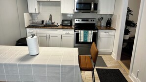 A modern kitchen with white cabinets, stainless steel appliances, and a dining area with a table and chairs. - Bright and spacious condo, a short walk to the beach, boardwalk and amusements.  (Wildwood)