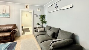 A living room with a grey sofa, a brown leather couch, a rug, and wall-mounted decor. - Bright and spacious condo, a short walk to the beach, boardwalk and amusements.  (Wildwood)