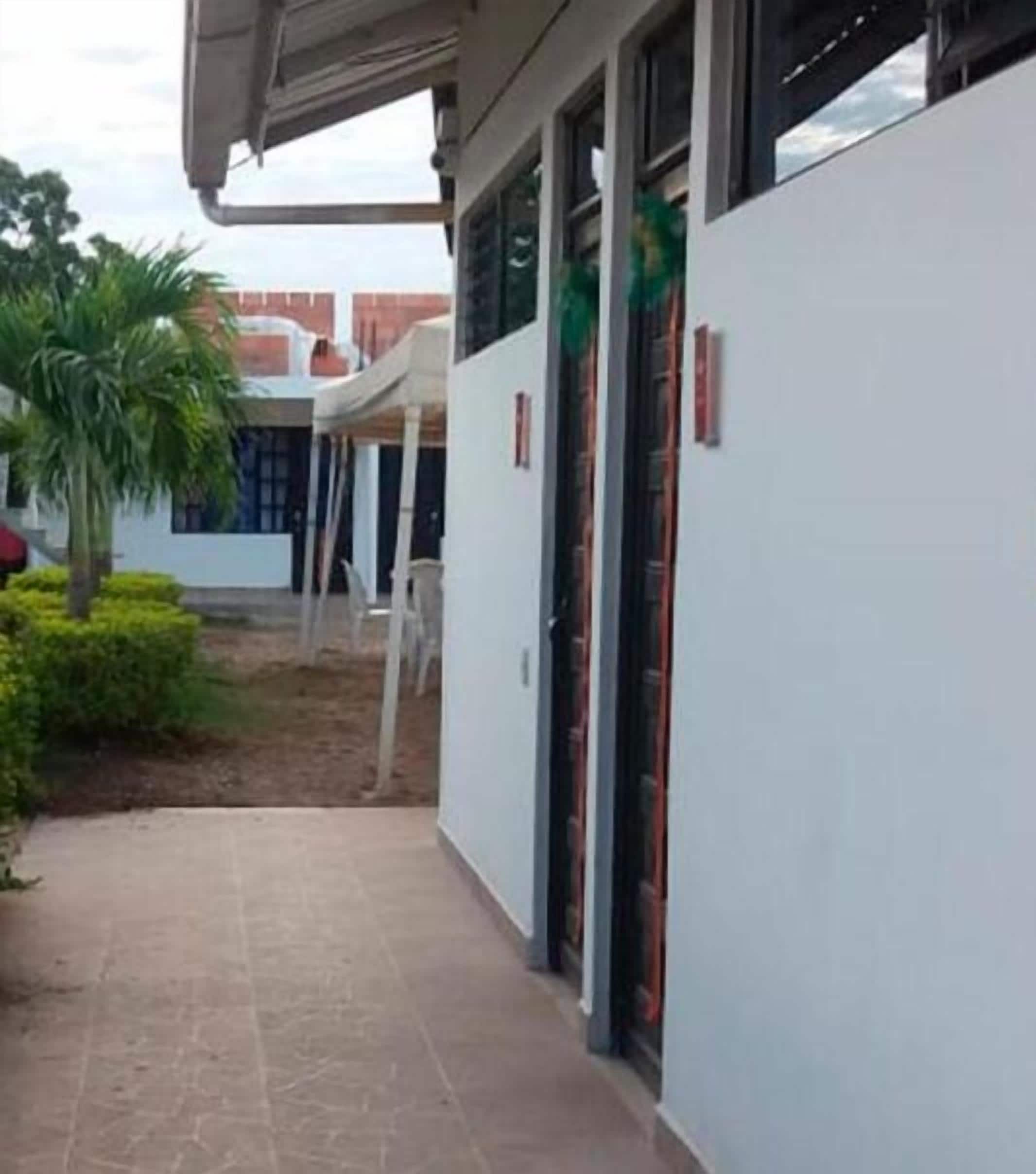 Un edificio con una galería techada, una palmera y una pared blanca con una puerta.