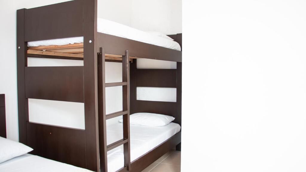 Una cama litera con escalera, ropa de cama blanca y estructura de madera.