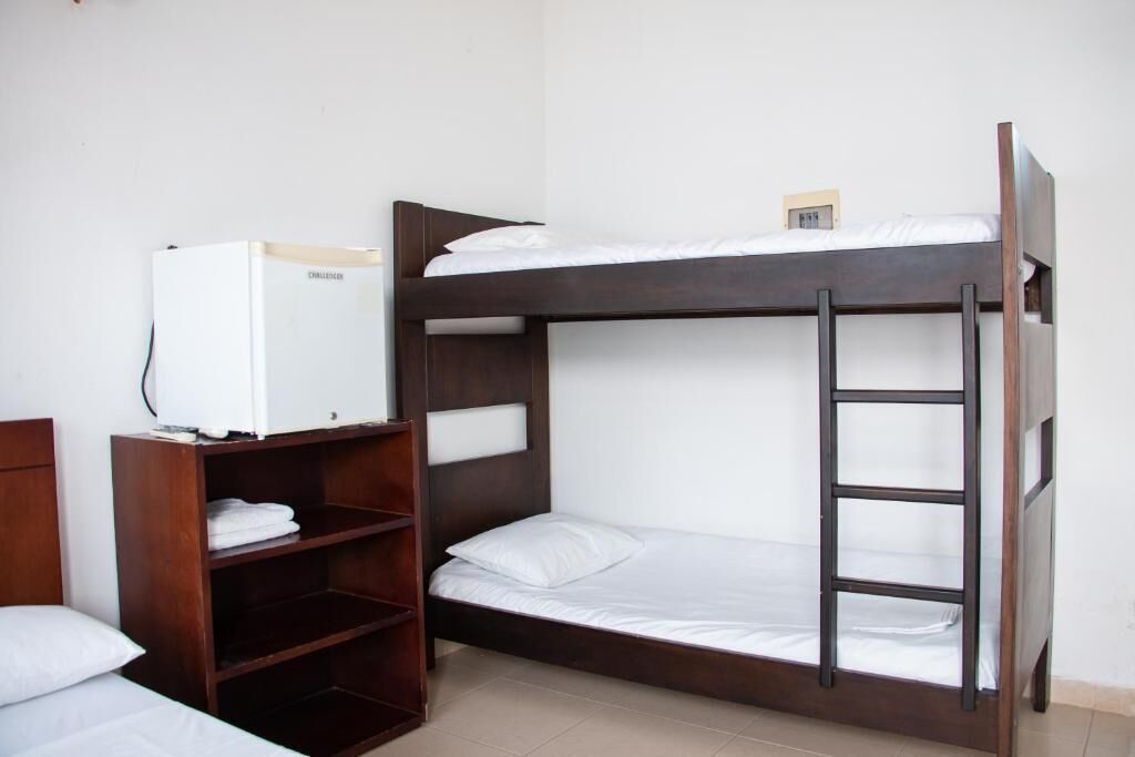 A bunk bed room with a wooden ladder, a small shelf unit, and a white refrigerator.