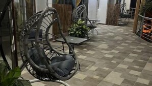 Un vaste espace extérieur doté d’un sol à carreaux, de fauteuils suspendus en osier et de plantes en pot.