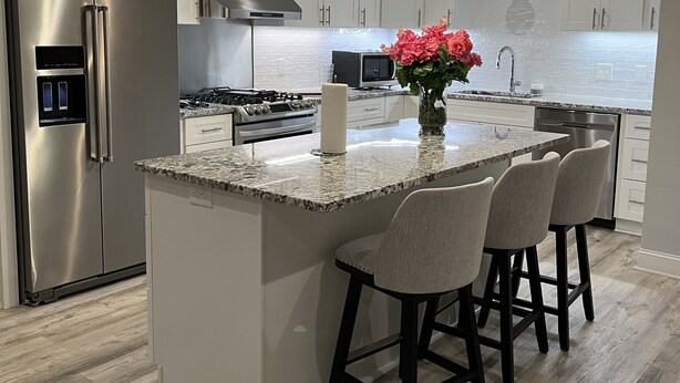 A modern kitchen with a stainless steel refrigerator, a gas stove, a microwave, and a sink. There is a large island with bar stools and a vase of flowers. - Modern meets country Loganville GA with AC, WiFi, pool. (Loganville)