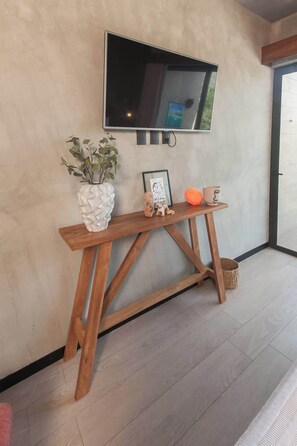 Une console en bois ornée d’un vase contenant des plantes vertes, d’un tableau encadré et de deux tasses.
