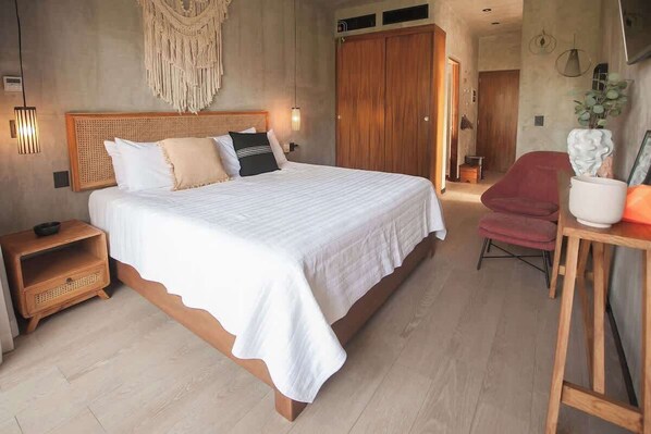 A bedroom with a large bed, wooden headboard, bedside tables, a red chair, and a wooden wardrobe.