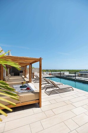 A rooftop terrace with a pool, lounge chairs, and a wooden pergola.