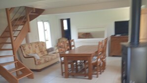 Ein Wohnzimmer mit einer Holztreppe, einem Sofa, einem Esstisch mit Stühlen und einem Kamin.