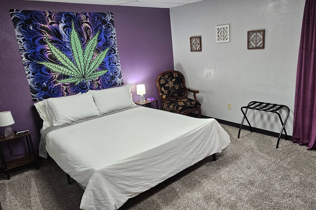 A hotel room with a bed, a chair, a small table, and a tapestry on the wall.