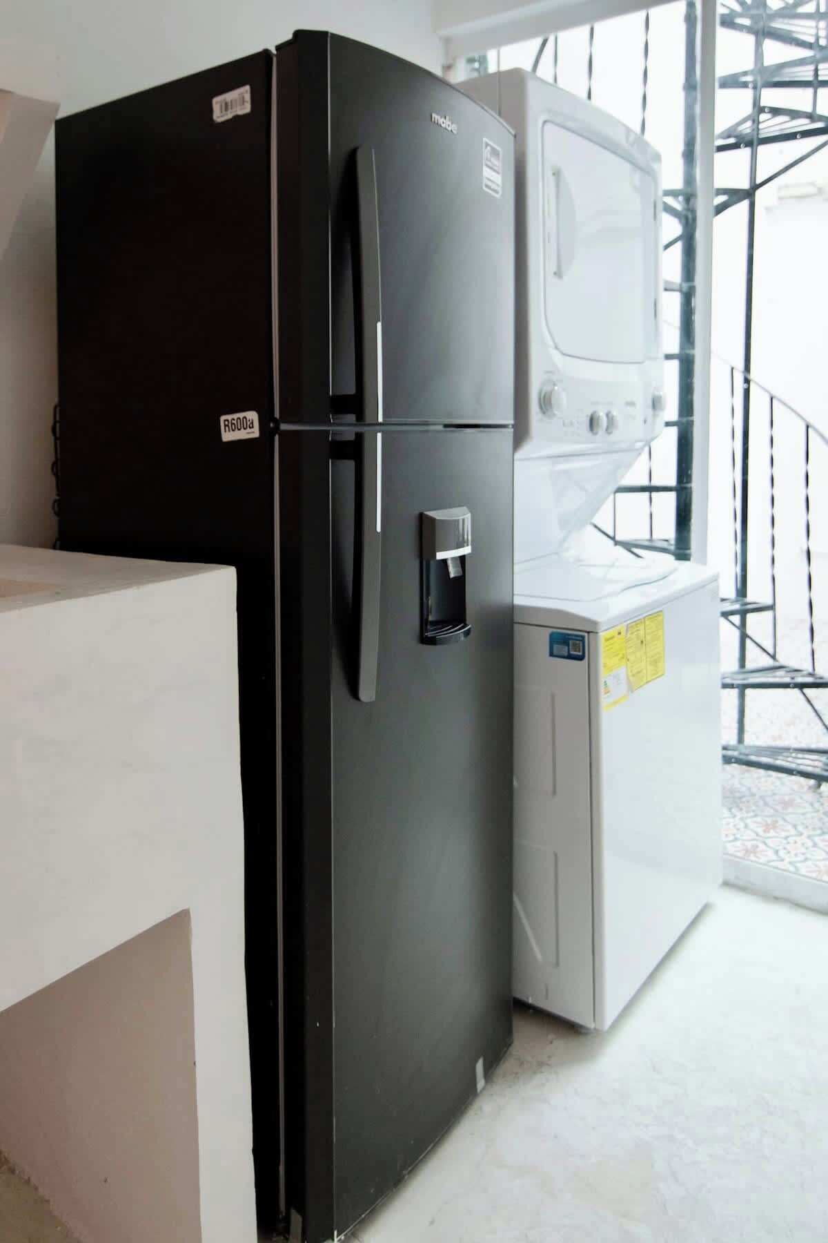 Een compacte keuken met een zwarte koelkast, een witte wasmachine en een wit aanrecht.