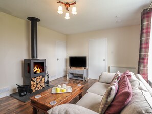 A cozy living room with a wood-burning stove, a television, a sofa, and a dining table. - Taigh Neilag (Strath)