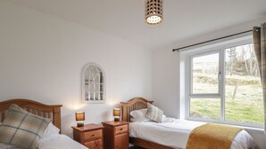 A bedroom with two beds, wooden nightstands, a window with a view of the outdoors, and a wall-mounted lamp. - Taigh Neilag (Strath)