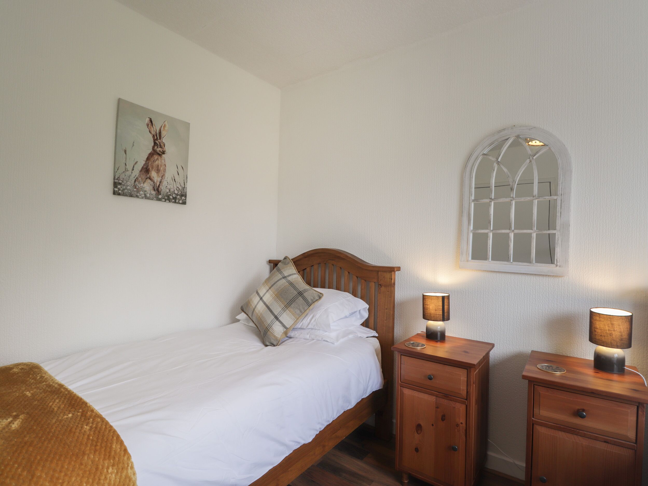 A bedroom with a wooden bed, a nightstand with a lamp, a small cabinet, and a window with a decorative frame.