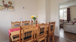 A dining area with a wooden table and chairs, a vase with flowers, and a painting on the wall. - Taigh Neilag (Strath)