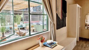 Ein modernes Zimmer mit einem großen Fenster, einem kleinen Tisch mit Blumenvase und einem an der Wand befestigten Regal.