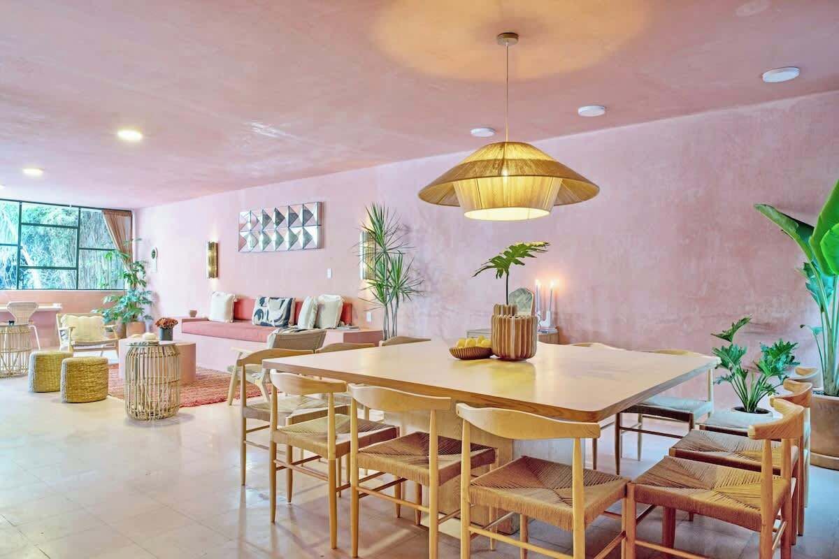 Een ruime woonkamer met een grote houten eettafel, rieten stoelen en een hanglamp.